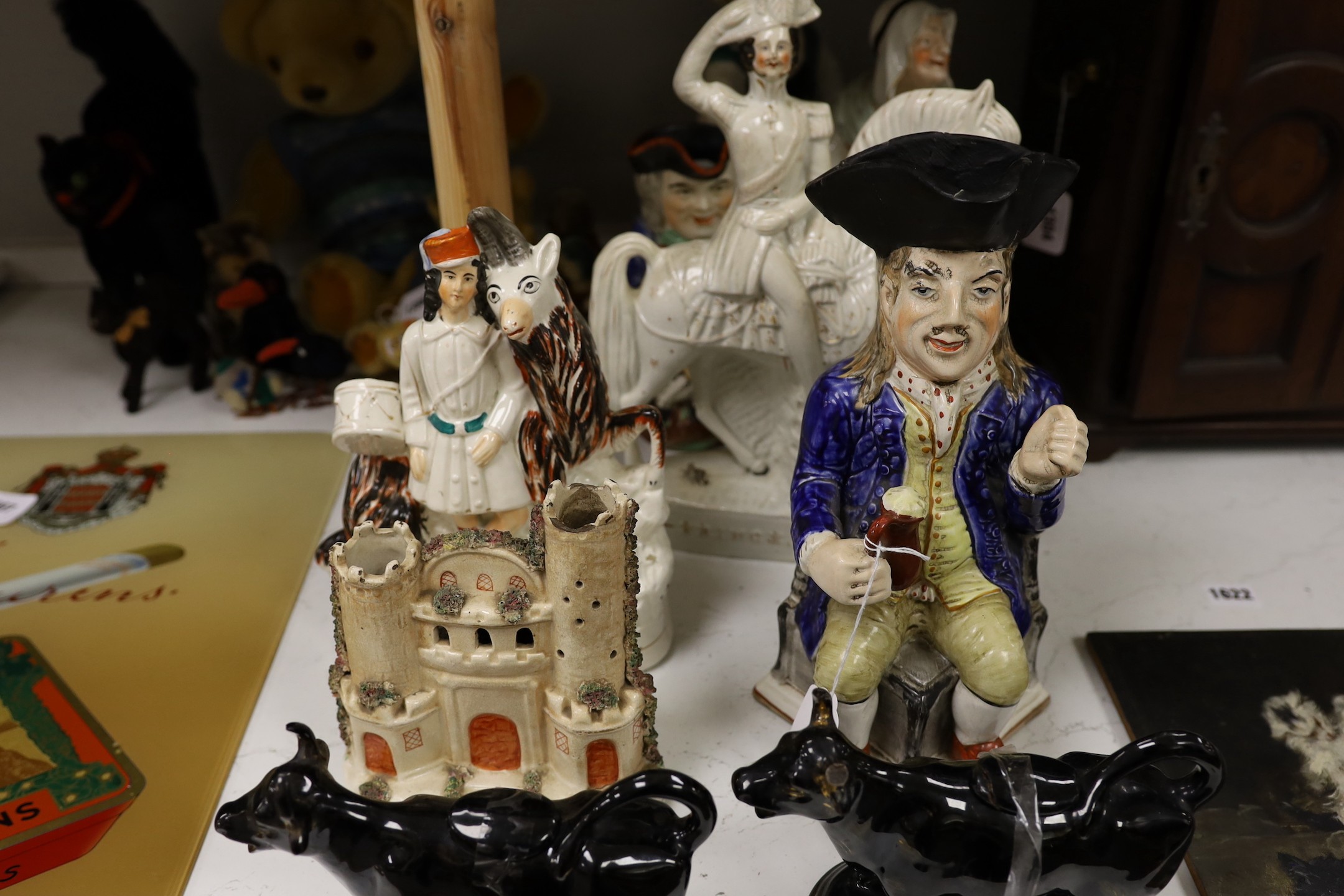 Five Staffordshire pottery figures or groups, tallest 36 cm high two similar Toby jugs, a pair of black glazed cow creamers and a model of a castle